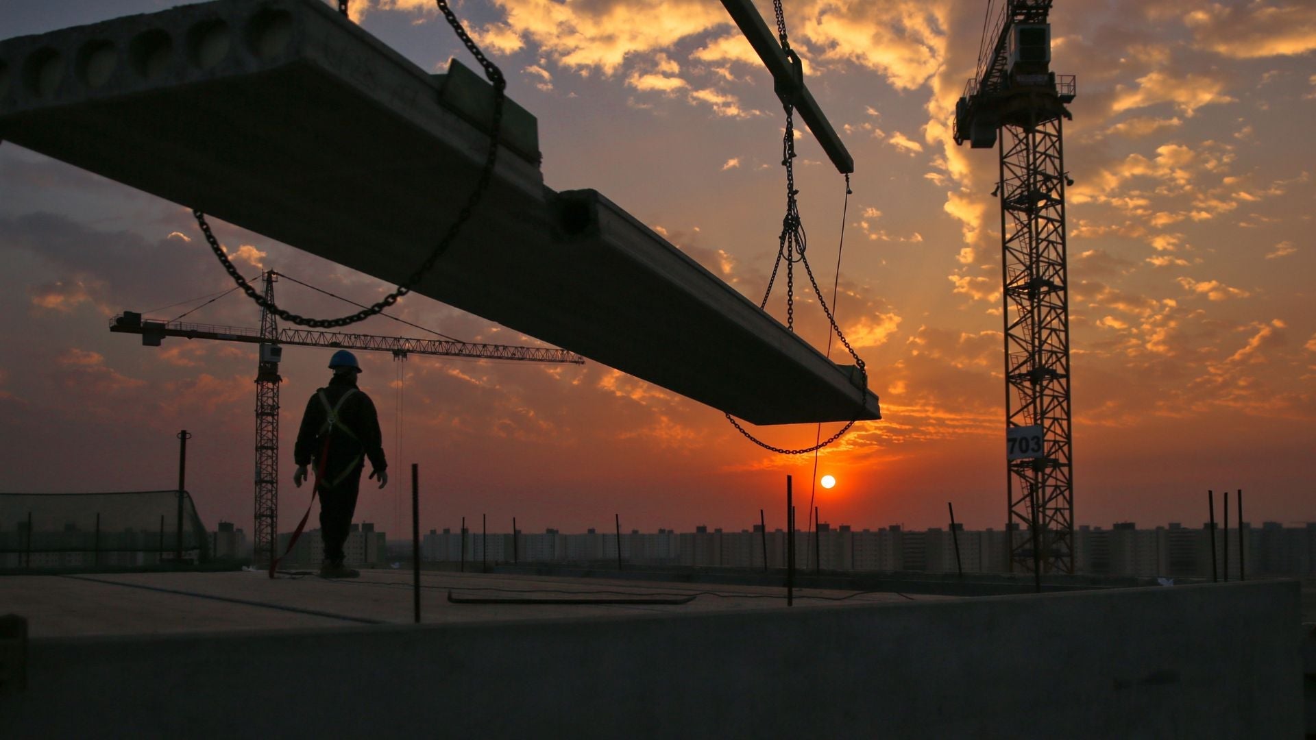 A construction site during a sunset. The image shows a crane and a person standing on a scaffolding. Construction sites can easily be secured with TurnIQ products.